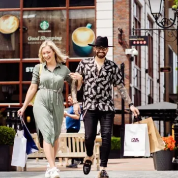 Twee mensen wandelen met winkeltassen door Designer Outlet Roermond tijdens Late Night Shopping.